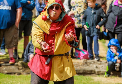 Man dressed as a jester juggling balls while an audience watches behind him